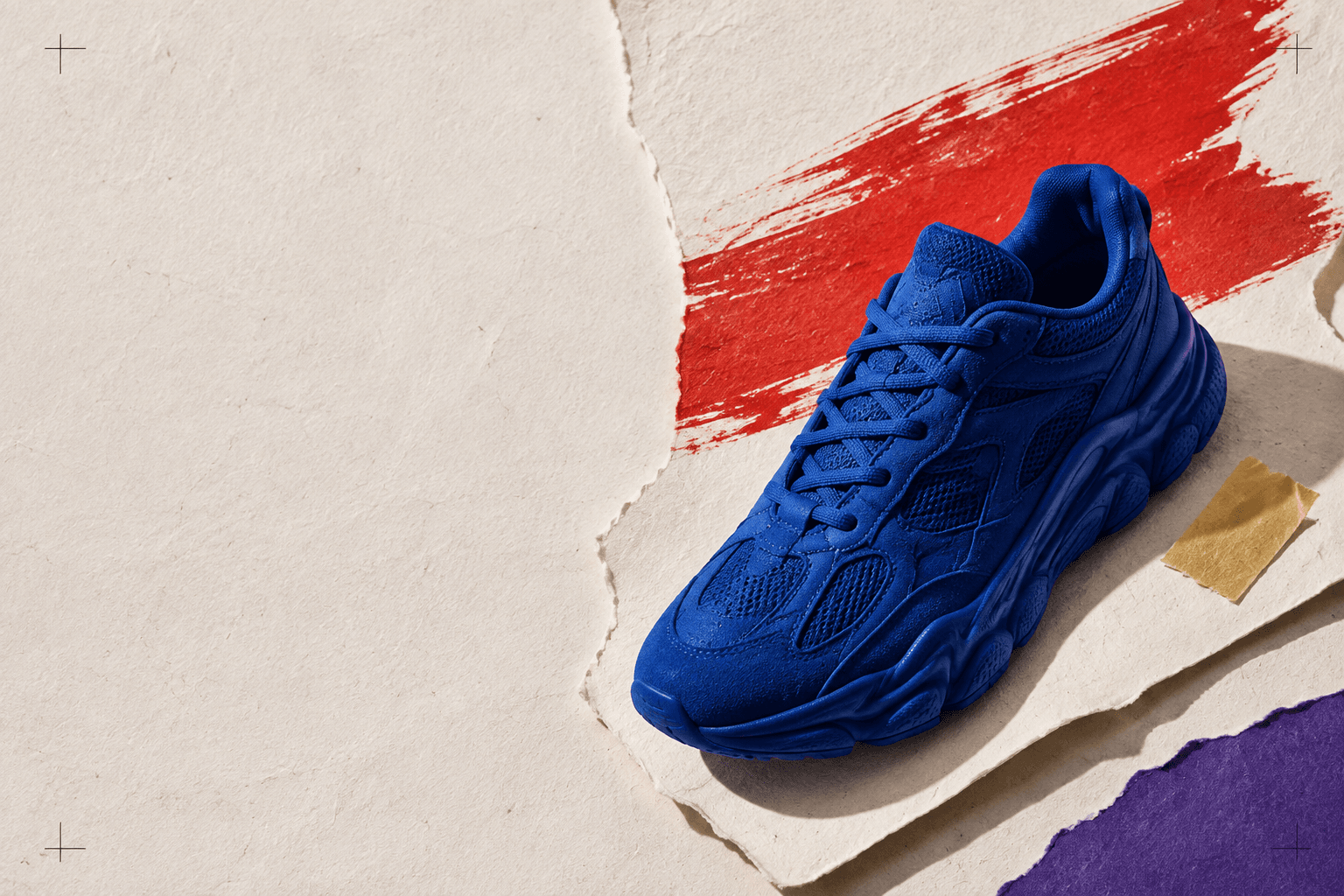 Cobalt blue sneaker on a collage of cream, red, purple and yellow paper